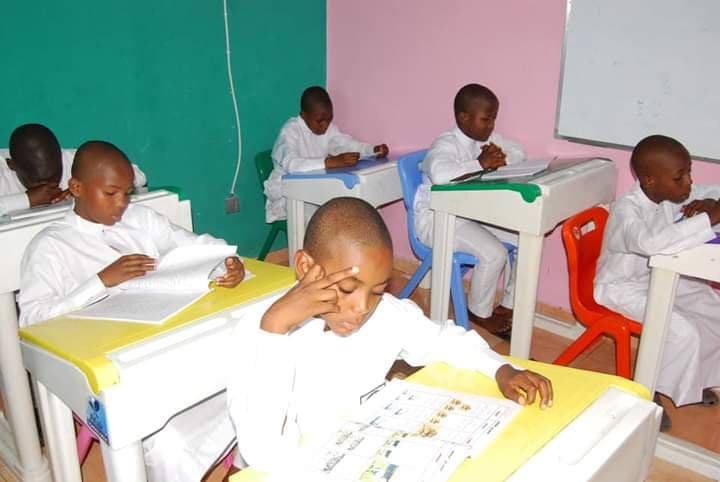 Primary boys in white thawb reading and writing at colourful desks