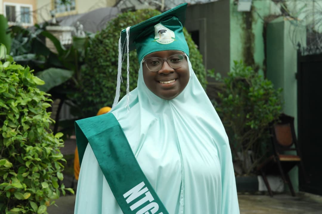 Smiling female graduate in green cap and gown with NTGA sash