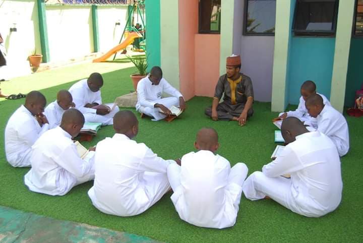 Students seated in a halaqah circle reading the Quran outdoors on green turf